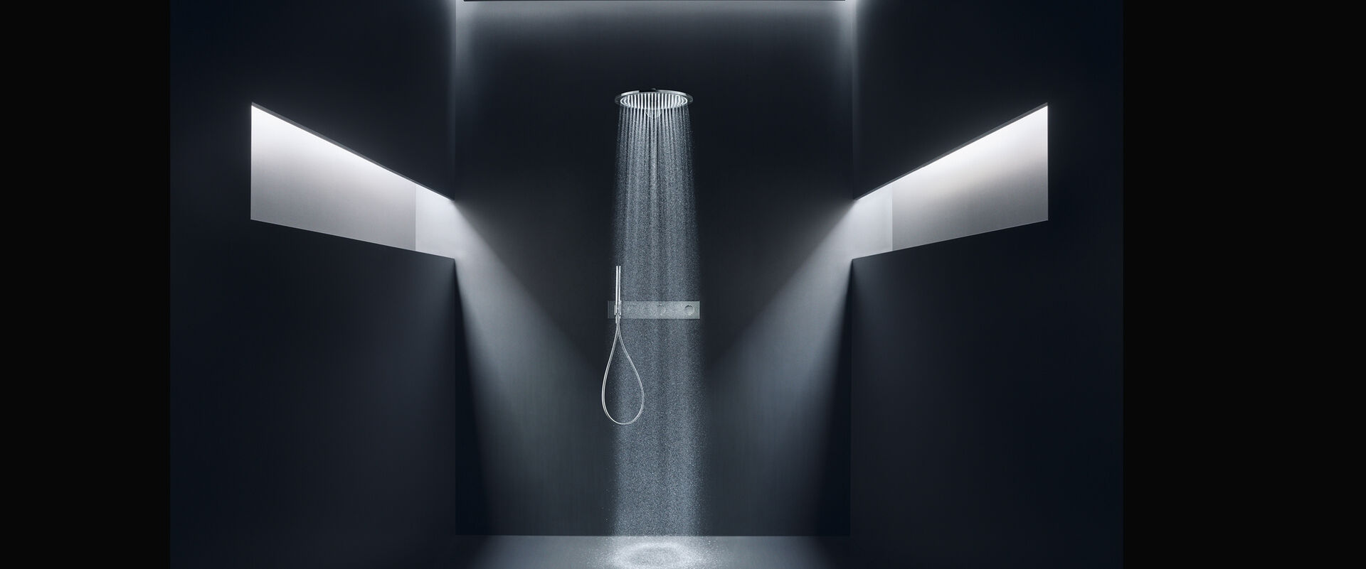 Elegantes Schwarzes Badezimmer, in dem eine Axor Showers Kopfbrause installiert ist. Lichtschächte Links und Rechts sorgen für eine geheimnisvolle Stimmung. Aus der Kopfbrause fließt das Wasser.