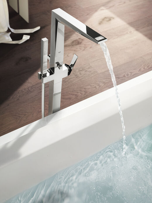 GROHE Allure Brilliant Badewannenarmatur mit Handbrause steht neben einer eckigen Badewanne.
