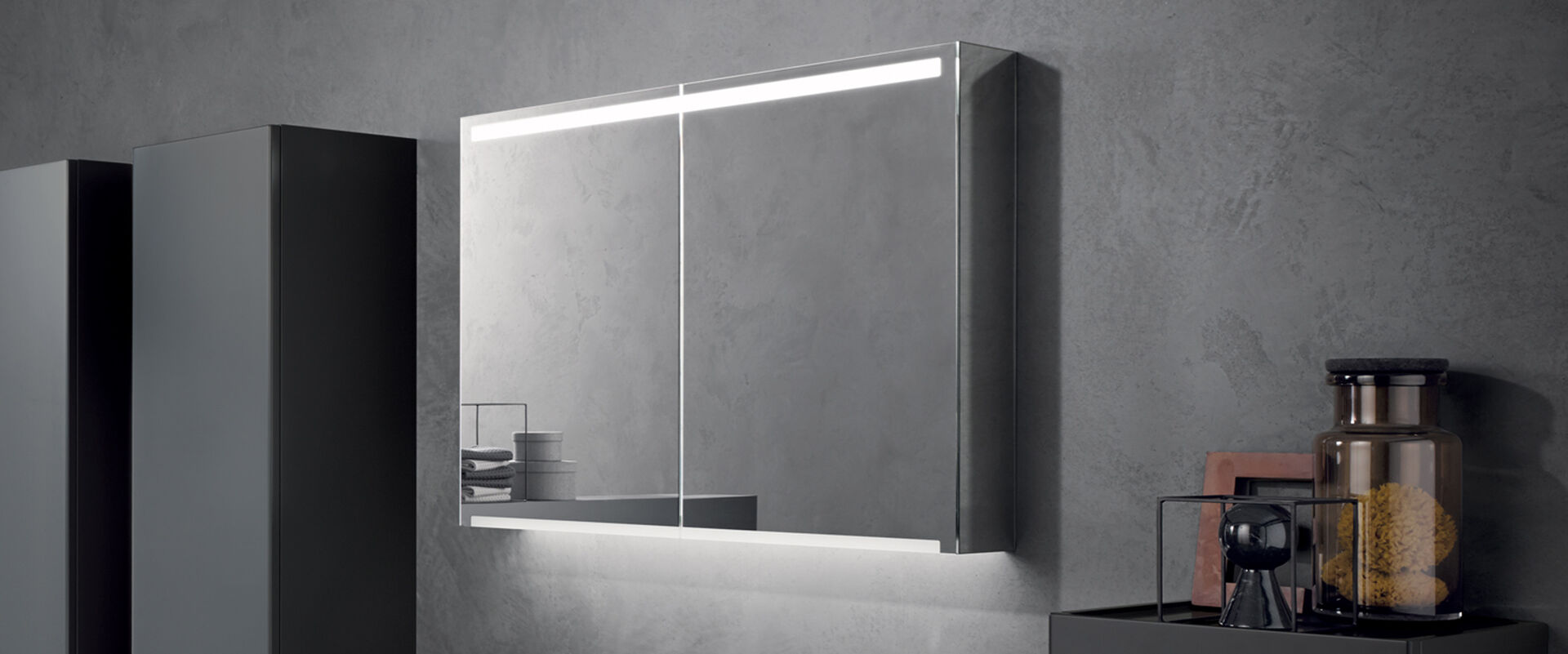 Doppelseitiger Spiegelschrank beleuchtet an einer grauen Wand.