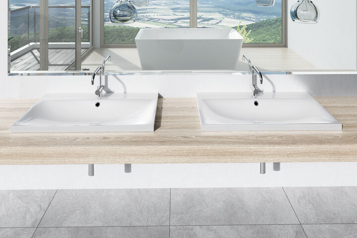 Zwei Waschbecken Silenio von Kaldewei, die auf einem hölzernen Waschtisch installiert sind. Darüber hängt ein Spiegel, in dessen Spiegelung eine weiße Badewanne zu erkennen ist.