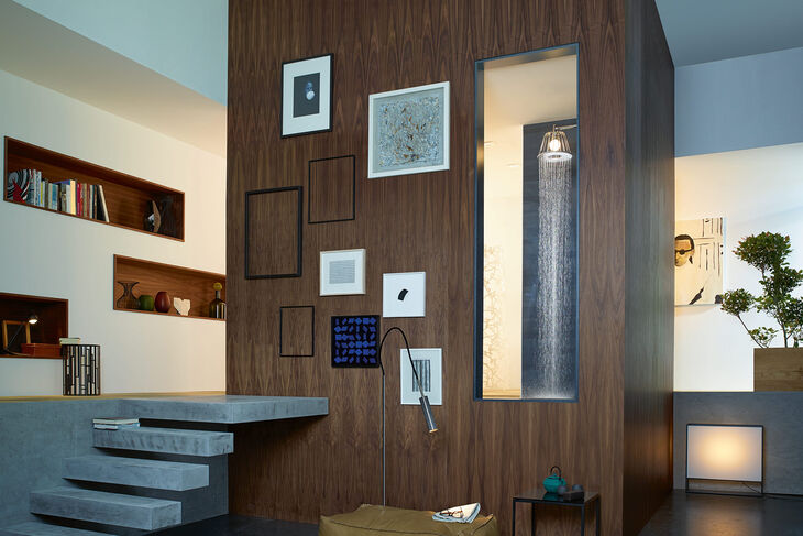 AXOR Lampshower by Nendo Große Duschkabine in einem stilvoll eingerichtetem Zimmer. Durch ein Fenster in die Kabine erkennt man eine AXOR Nendo Lampshower, aus der Wasser fließt.