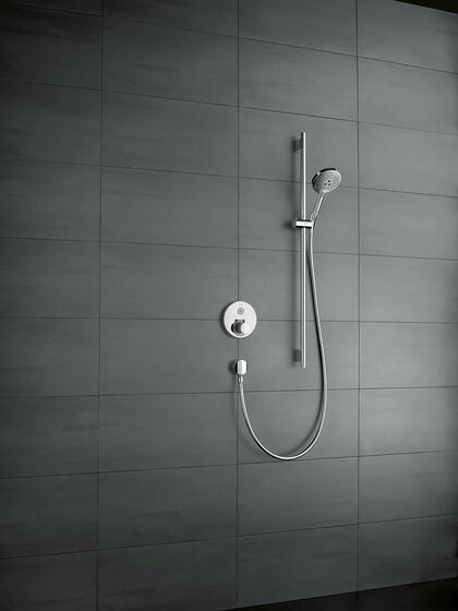 Grau geflieste Duschwand, an der ein rundes hansgrohe ShowerSelect Thermostat befestigt ist, sowie eine Duscharmatur mit Handbrause. 