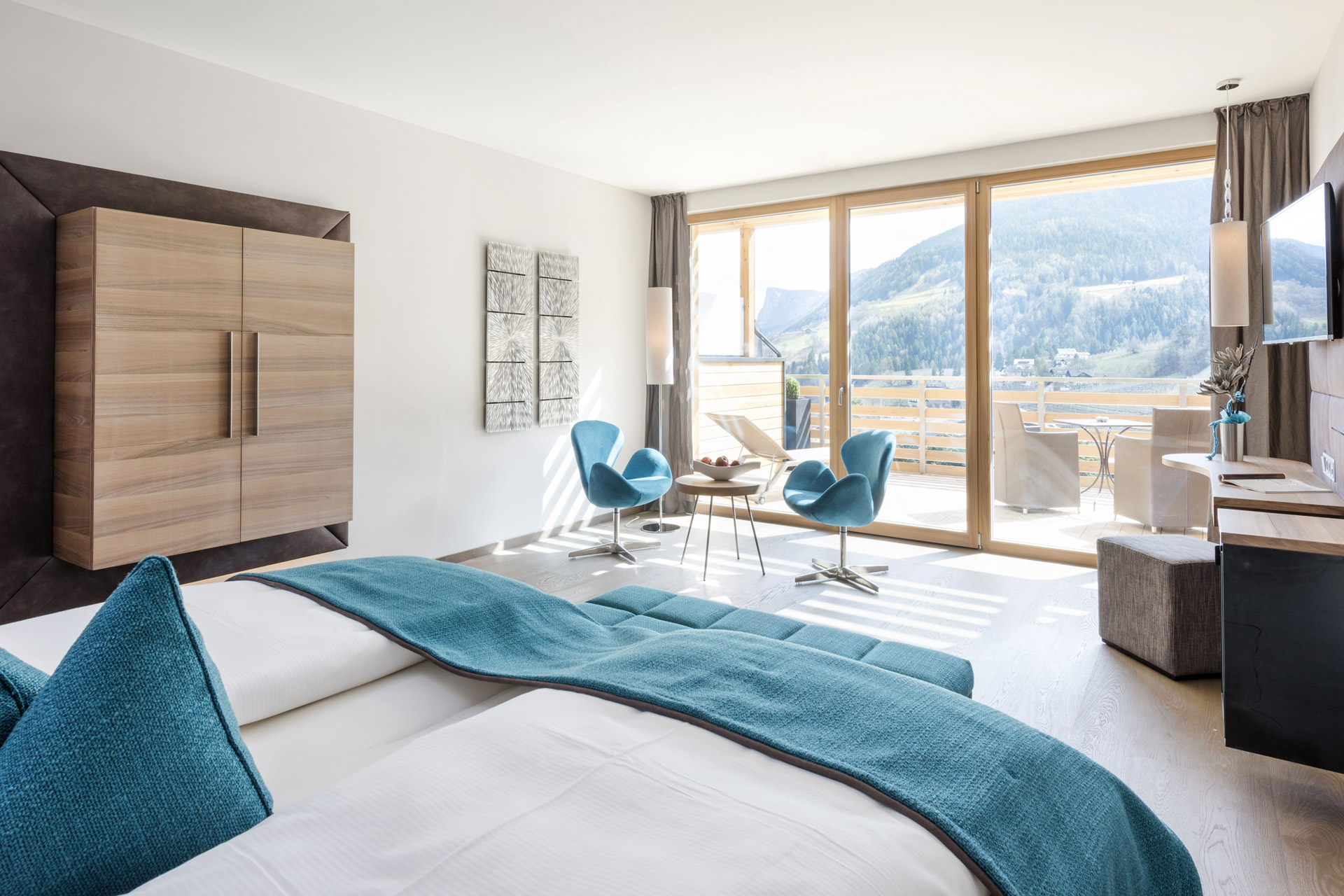Suite mit Balkon Alpiana Resort. Wandmontierter holzschrank seitlich, Doppelbett, Flat-TV und Sessel.
