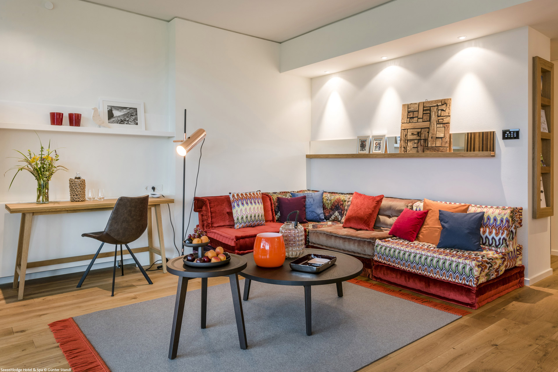 Wohnbereich in Suite Seezeitlodge mit bunter Sitzecke und einem Schreibtisch aus Holz seitlich.